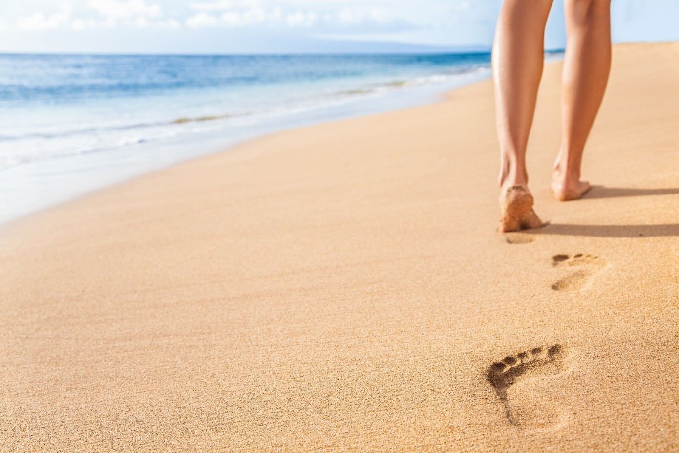 Close up of the back of a woman’s legs as she walks down a beach