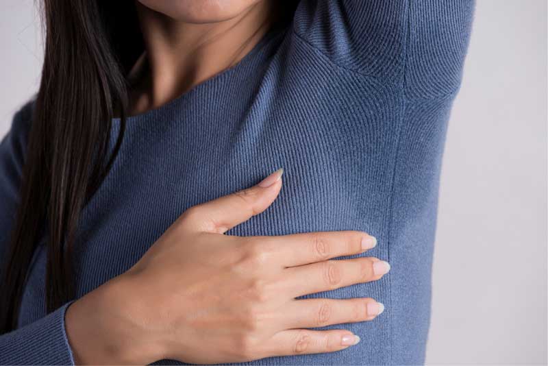 Young woman with sweat stain on her clothes against grey background, caused by excessive sweating condition hyperhidrosis